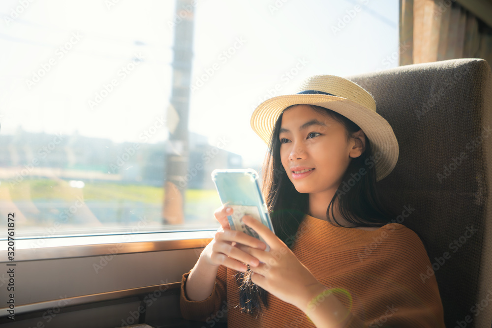 年轻的亚洲女旅行者在火车上使用智能手机。女旅行者拿着手机微笑