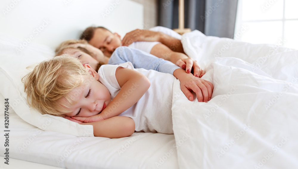 健康的睡眠。幸福的家庭父母和孩子睡在白色的床上。
