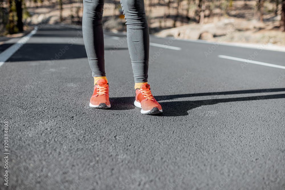 Sports woman in running shoes standing on the asphalt mountain road, close-up on sneakers