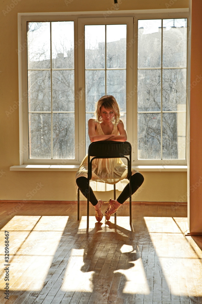 美丽的年轻女孩模特坐在靠近大窗户的大房间里