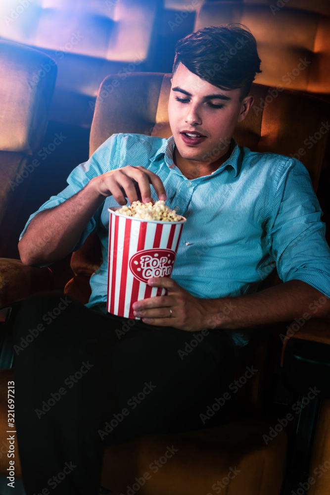一个年轻人在电影院看电影时，微笑着拿着爆米花享受