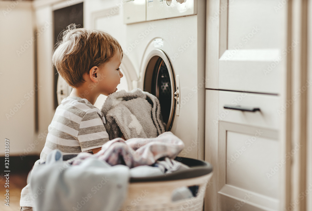 快乐的户主小男孩在洗衣房里用洗衣机。