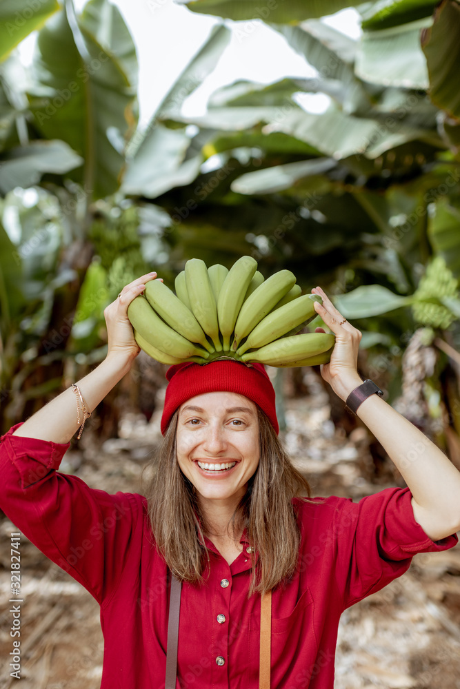 一个可爱微笑的女人的肖像，头顶着一根新鲜的绿色香蕉茎。健康饮食