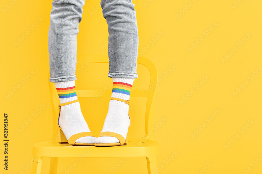穿着袜子和凉鞋的年轻女子站在彩色背景下的椅子上的腿