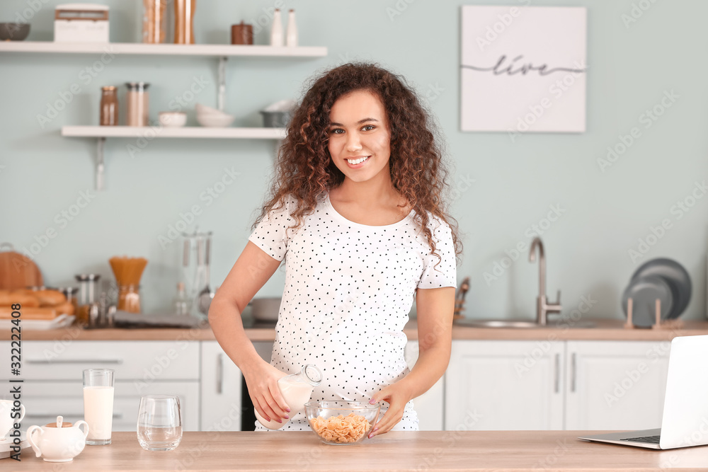怀孕的非裔美国妇女在厨房里喝牛奶和吃薯片
