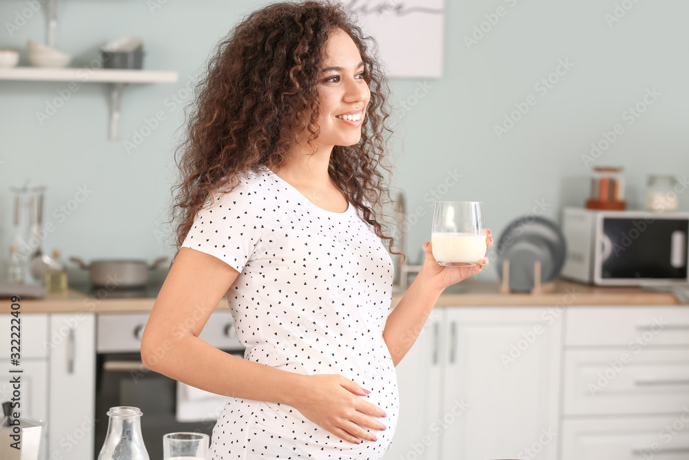 怀孕的非裔美国妇女在厨房喝牛奶