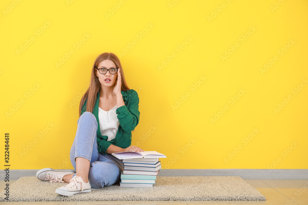 震惊的年轻女子拿着书坐在彩色墙附近