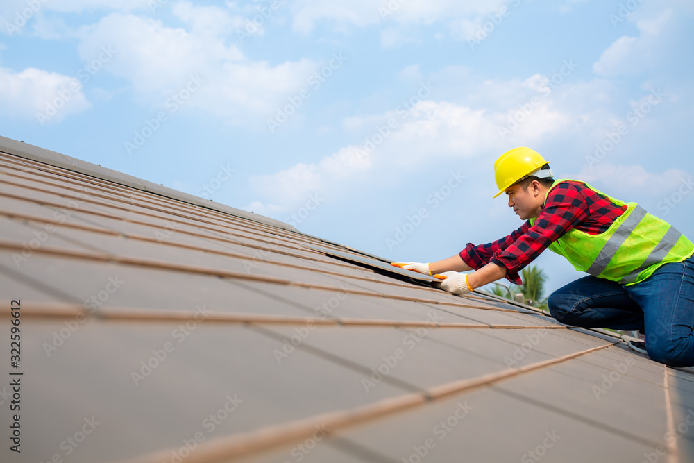 建筑工人安装屋顶维修，用安全工具包将屋顶瓷砖固定在有蓝天的房子上