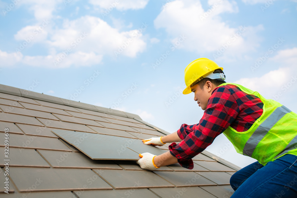 建筑工人安装屋顶维修，用安全工具包将屋顶瓷砖固定在有蓝天的房子上