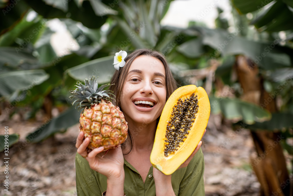 热带种植园里，一个年轻微笑的女人拿着木瓜片和ananas的画像。