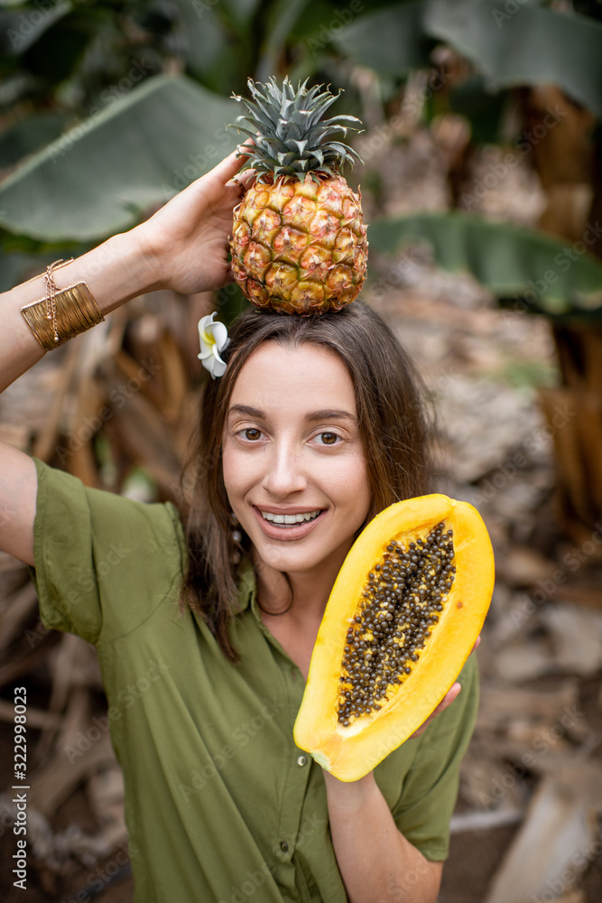 一个年轻微笑的女人的有趣画像，她拿着木瓜片和ananas在户外的热带植物上
