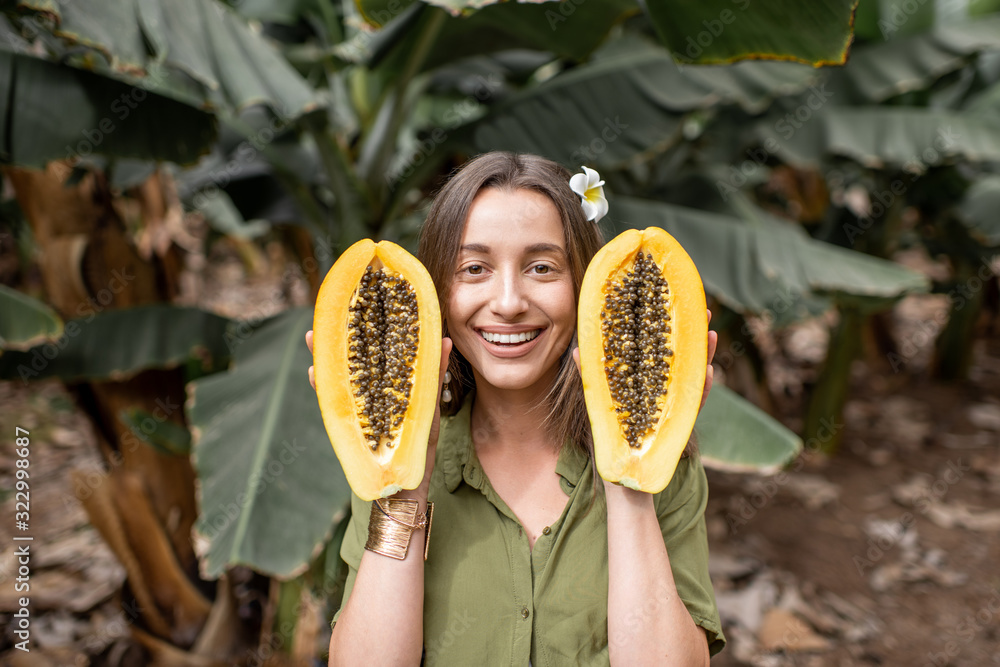 种植园里一个年轻女人拿着木瓜切片的肖像。素食主义的概念，治愈