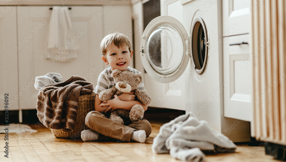 快乐的户主小男孩在洗衣房里用洗衣机。