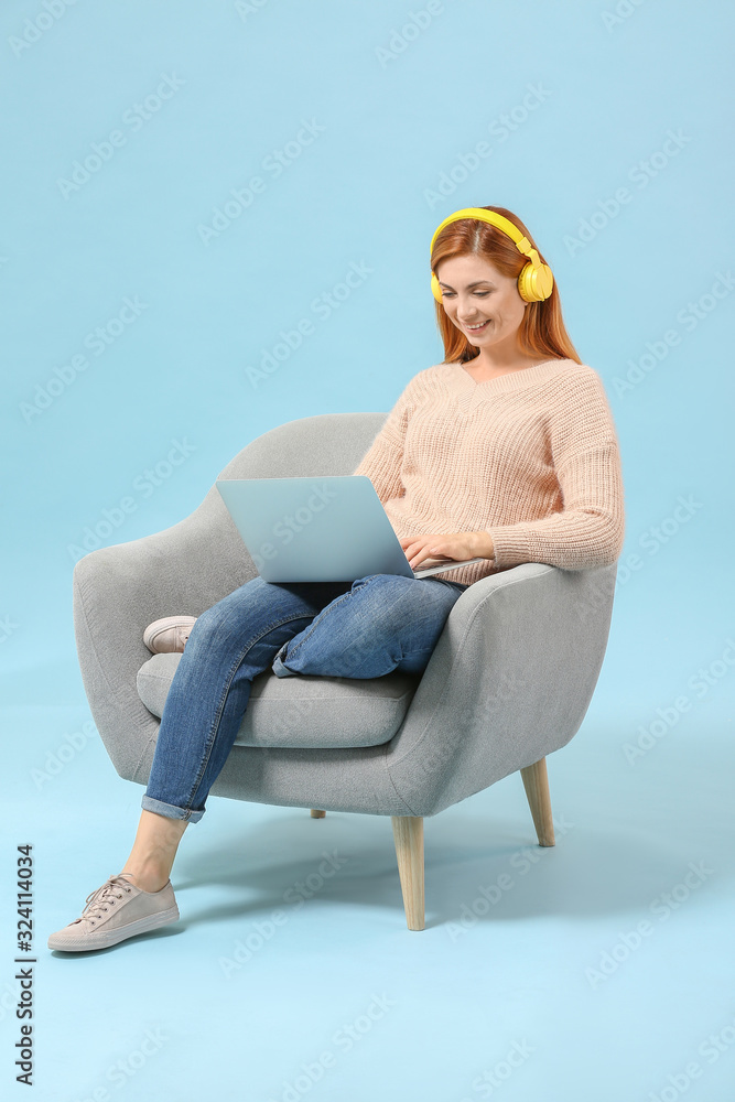 漂亮女人，拿着笔记本电脑，坐在彩色背景的扶手椅上听音乐