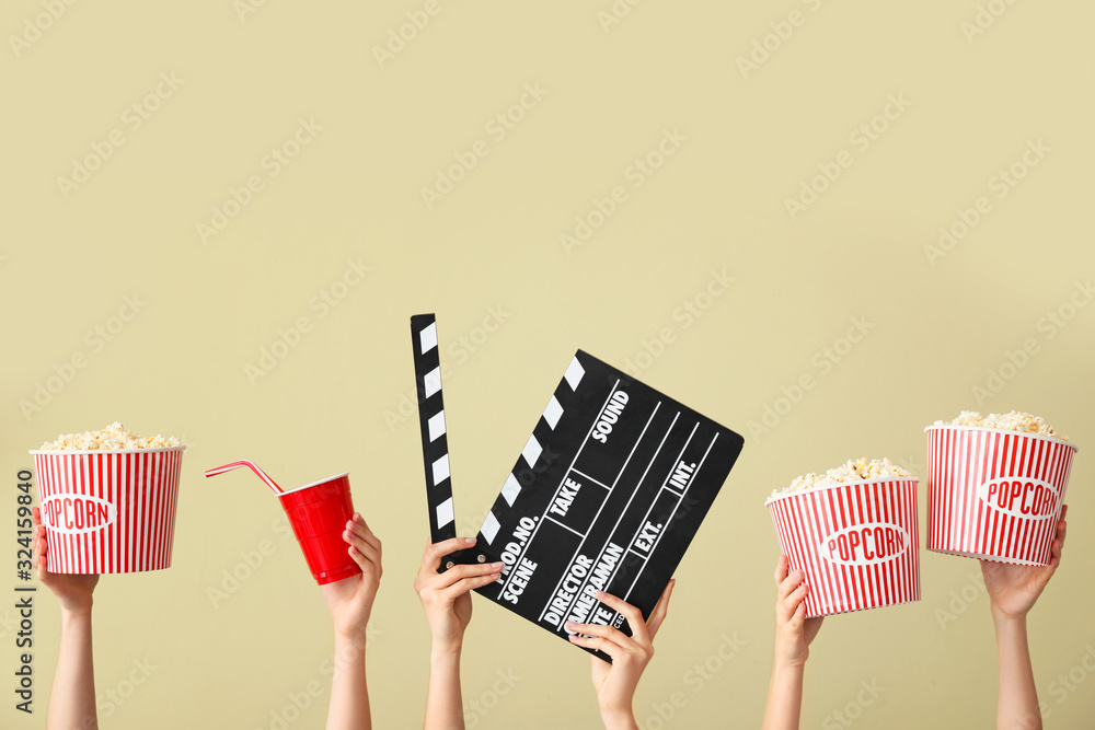 Many hands with popcorn, drink and movie clapper on color background