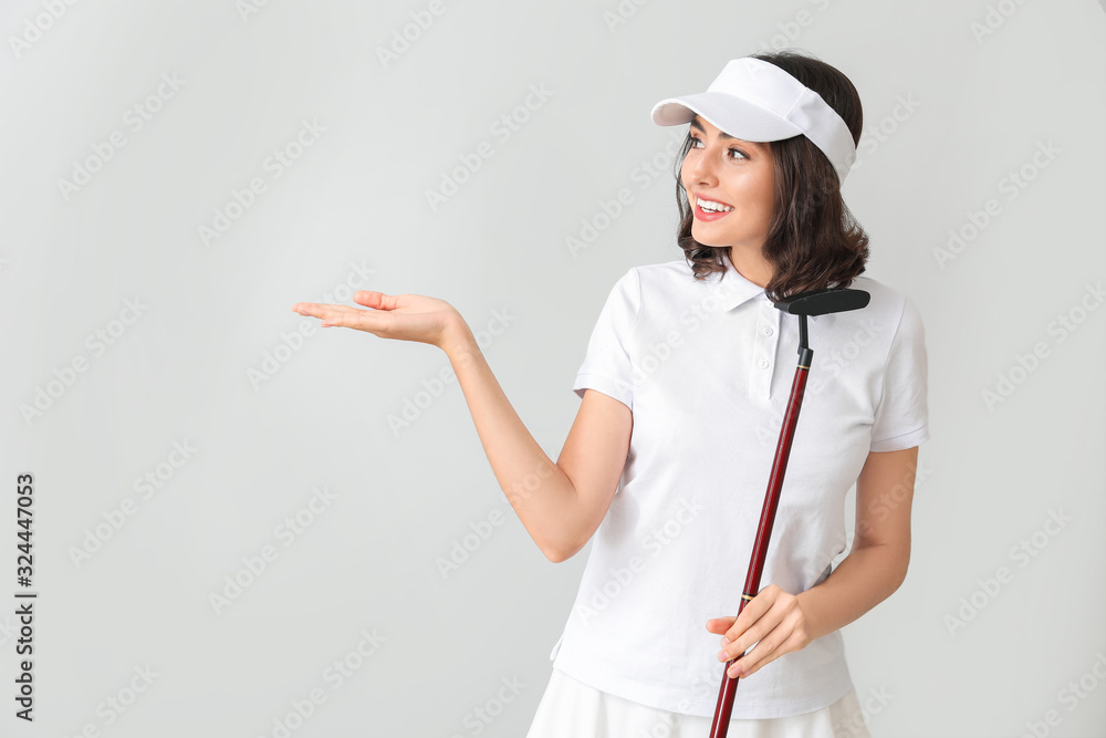 Beautiful female golfer showing something on light background