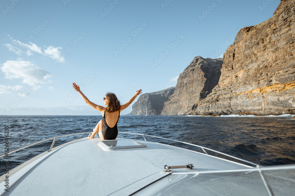 一名女子在惊险的岩石附近航行时，坐在游艇机头上享受海上航行