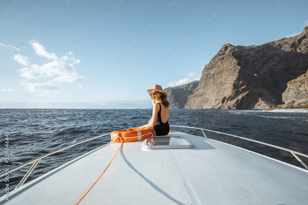 Woman enjoying ocean voyage sitting with lifebuoy on the yacht nose while sailing near the breathtak
