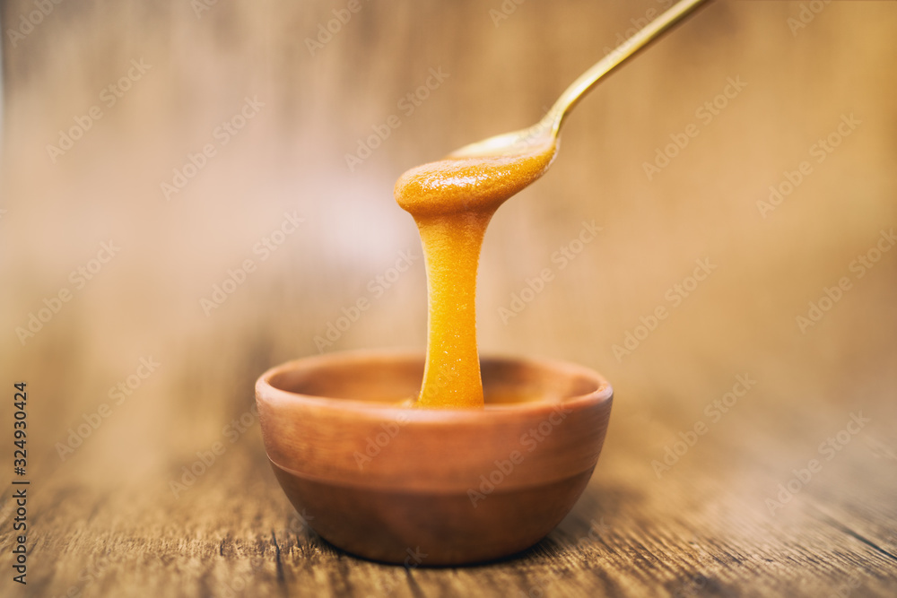麦卢卡蜂蜜勺浸在木质背景上的金色液体天然超级食物中。