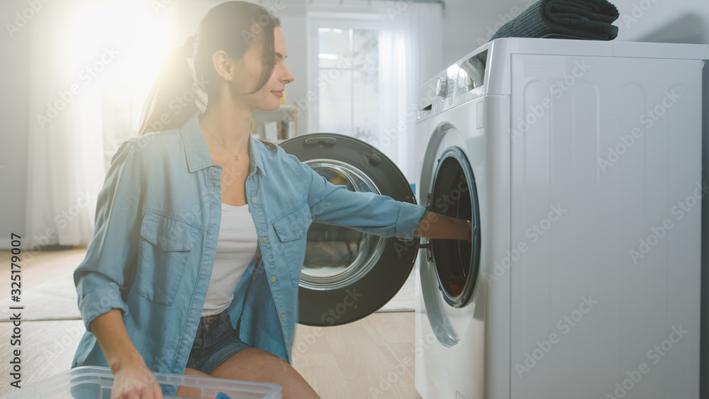 Beautiful Smiling Brunette Young Woman Sits in Front of a Washing Machine in Homely Jeans Clothes. S
