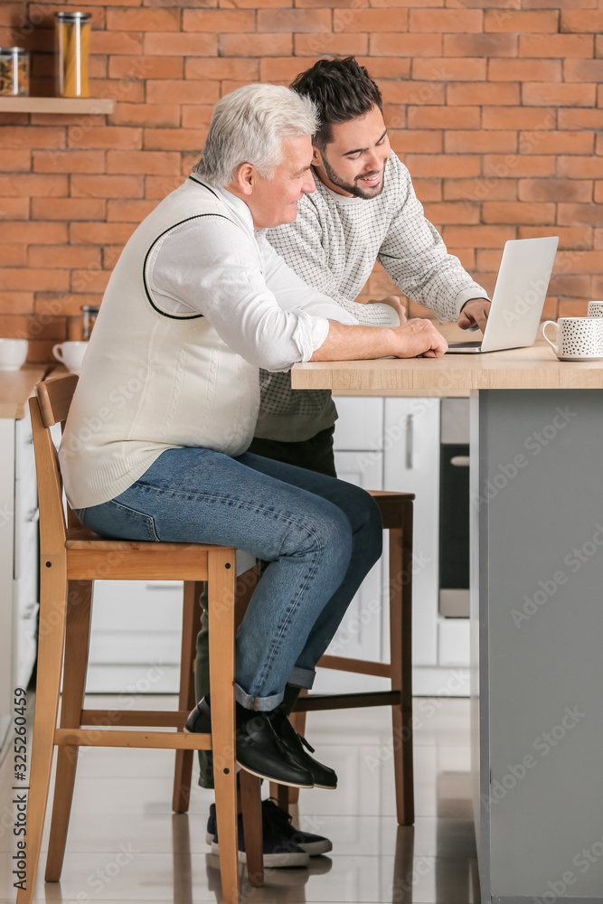 年轻人和他的父亲在厨房里拿着笔记本电脑