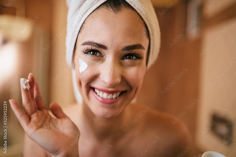 年轻快乐的女人在浴室里脸上涂润肤霜。