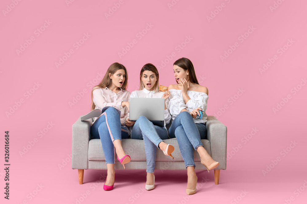 用笔记本电脑坐在彩色背景的沙发上，让年轻女性大吃一惊。网上购物概念