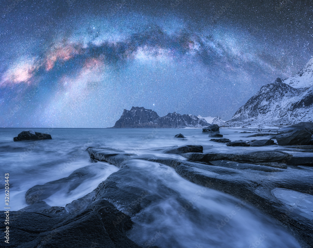挪威罗弗敦群岛冬季夜晚白雪覆盖的山脉和岩石海滩上的银河