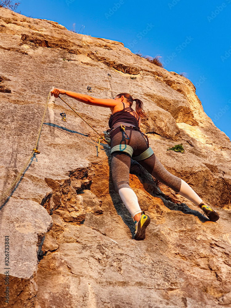 垂直：在一个阳光明媚的夜晚，无法辨认的女性攀岩者爬上墙壁。