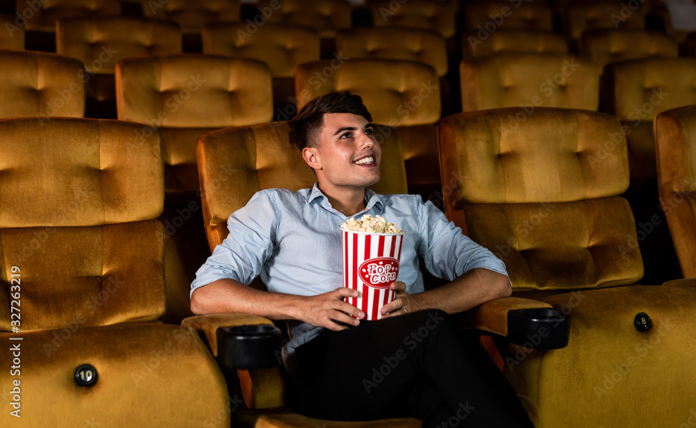 一个年轻人在电影院看电影时，微笑着享受着爆米花
