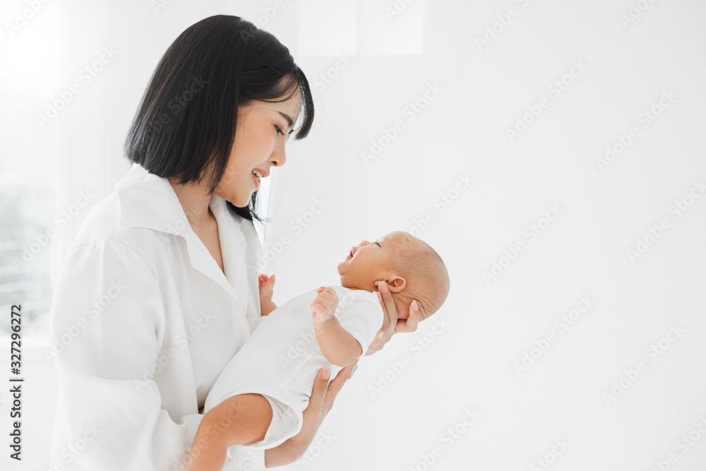 年轻的亚洲母亲在白色的床上用爱抱着她的新生儿，母亲节的概念