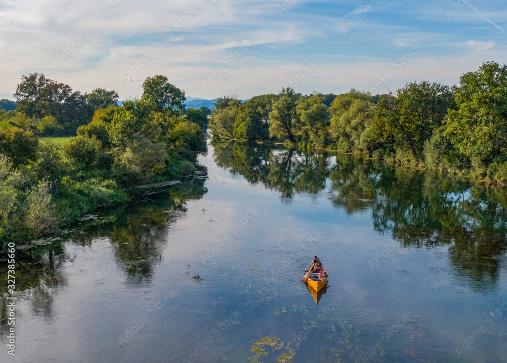 DRONE: Young man paddles canoe along a tranquil river while his friends relax.