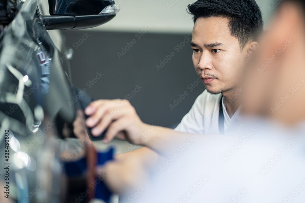 两名亚洲汽车贴膜保护男工人在车库为黑色汽车安装贴膜。男子关注ho
