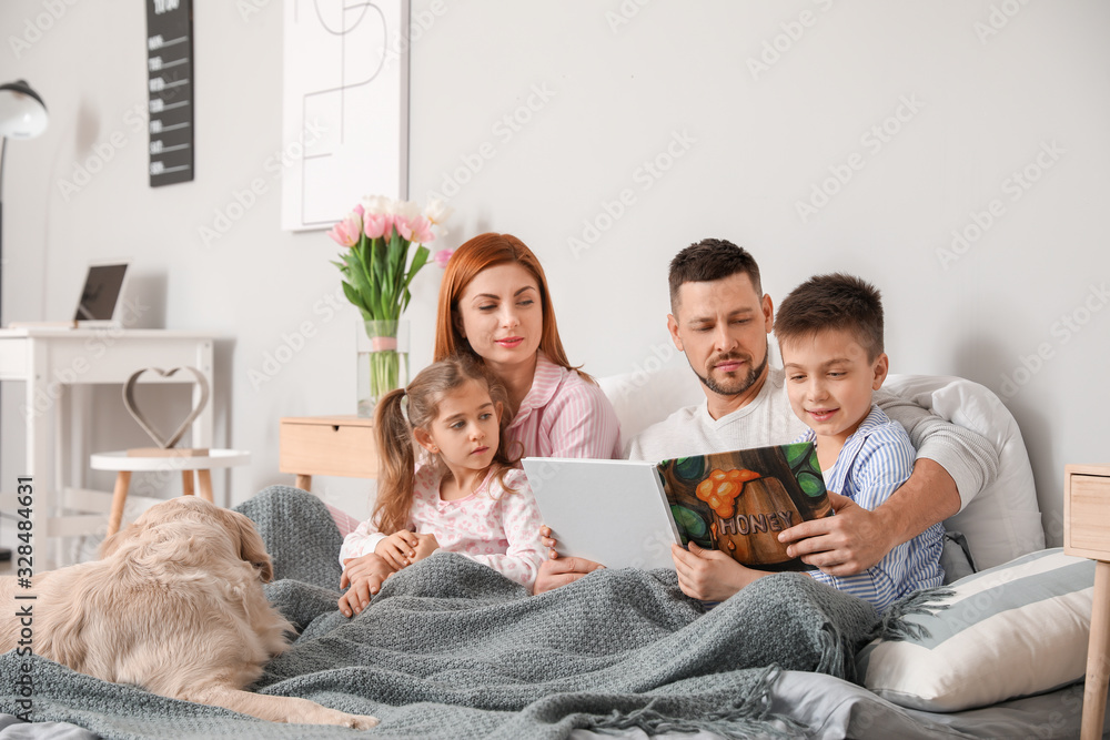 Happy family with dog reading book in bedroom at home
