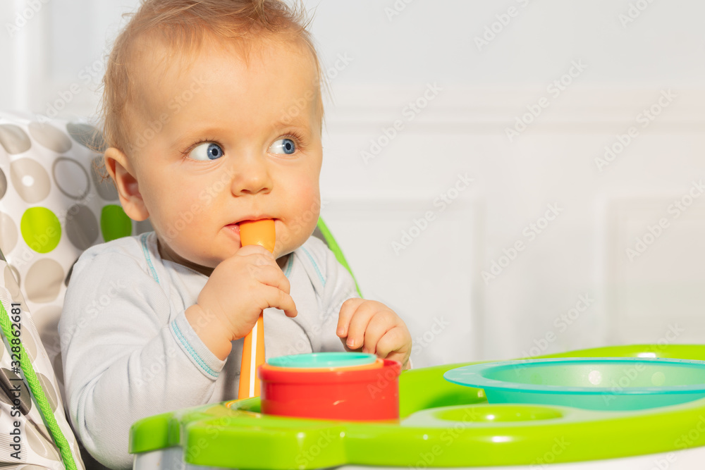 蹒跚学步的男婴坐在高脚椅上，拿着塑料勺子，若有所思