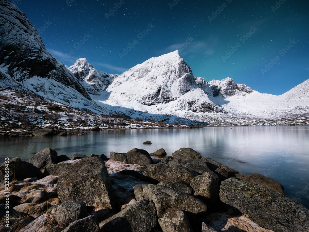 Mountains and reflections on water at night. Winter landscape. The sky with stars and clouds in moti