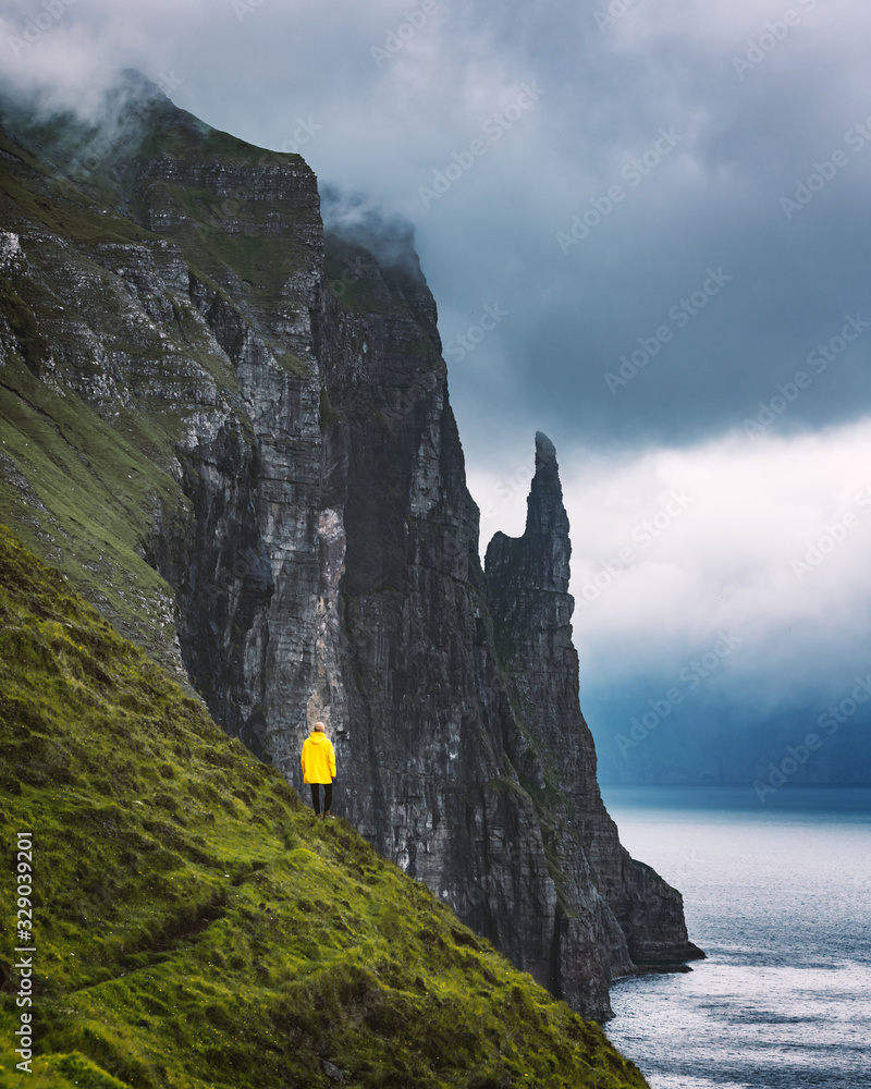 穿着黄色夹克的游客从Trollkonufingur的角度观看Witches Finger悬崖。Vagar岛