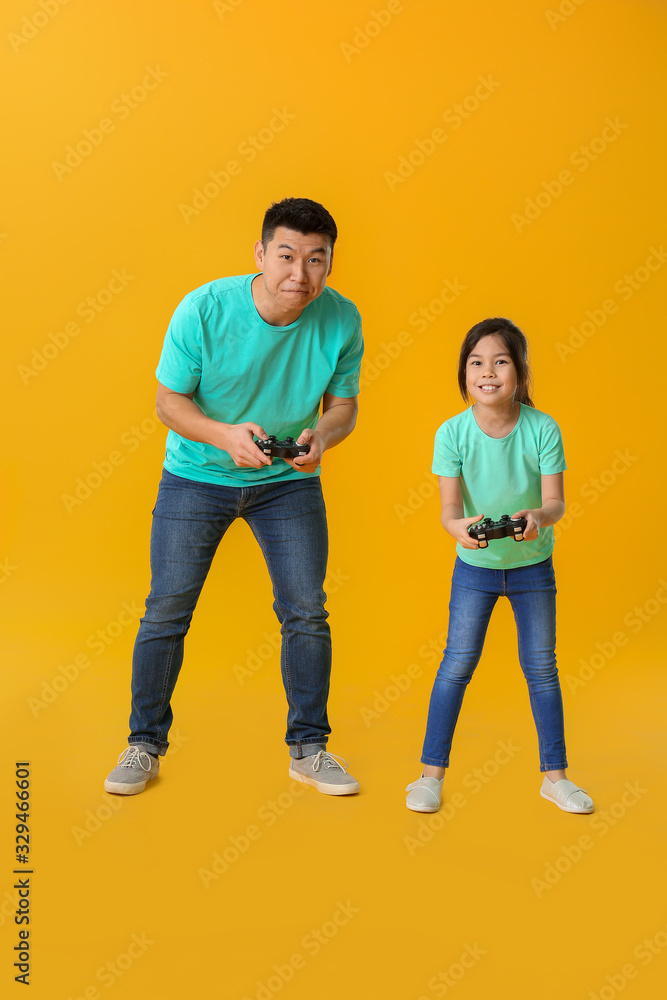 亚洲男子和他的小女儿在彩色背景下玩电子游戏