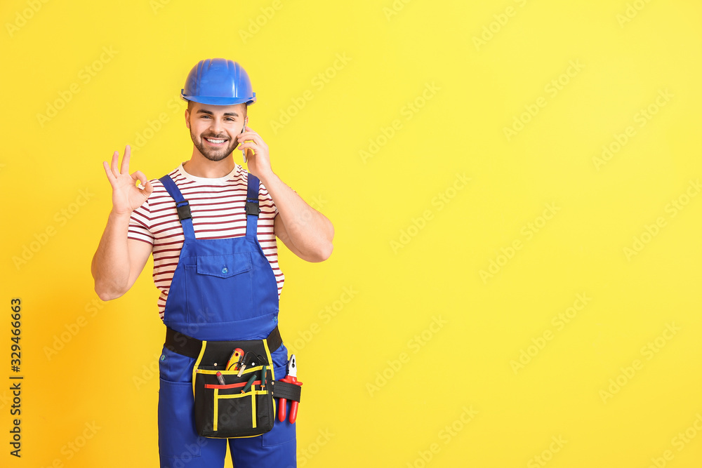 Male worker talking by mobile phone on color background