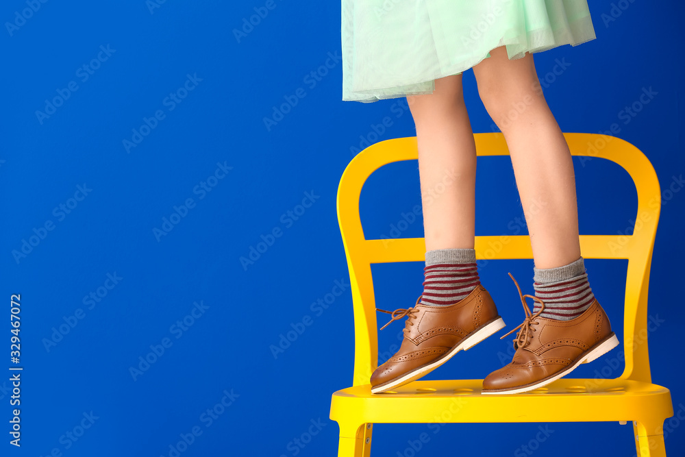 小女孩站在彩色背景下的椅子上