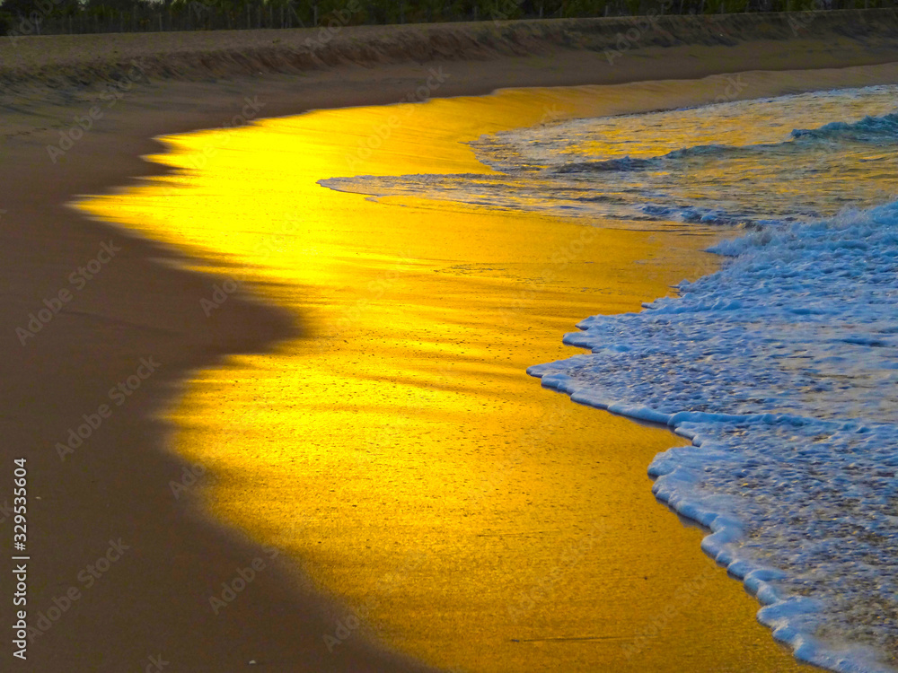 特写：金色日落时，温暖的海水冲刷着空旷的沙滩。
