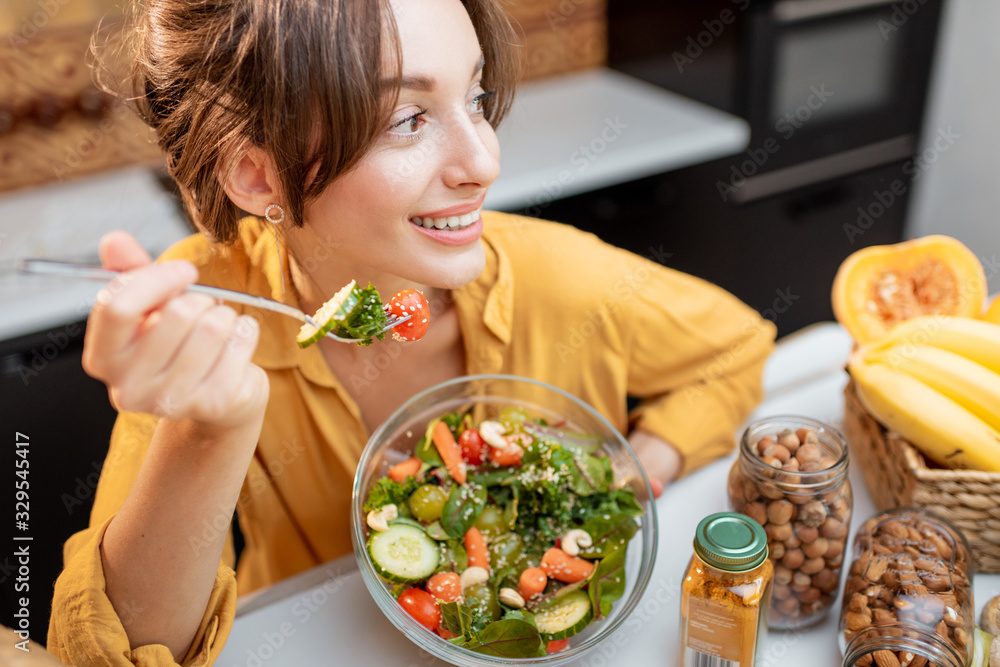 一个年轻快乐的女人在餐桌上吃沙拉的画像，餐桌上摆满了健康的生蔬菜和油炸食品