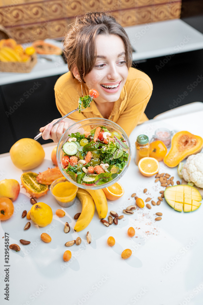 一位年轻开朗的女士在餐桌上吃沙拉的画像，餐桌上摆满了健康的生蔬菜和油炸食品