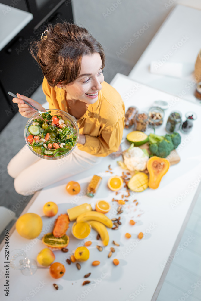 一个年轻快乐的女人在餐桌上吃沙拉的画像，餐桌上摆满了健康的生蔬菜和油炸食品