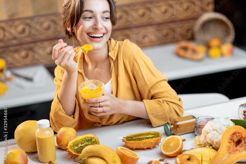 Young and cheerful woman eating chia pudding, having a snack or breakfast in the kitchen with lots o