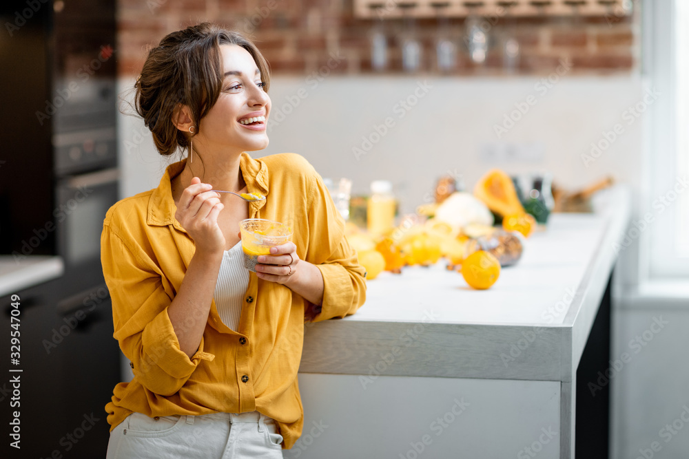 Portrait of a young and cheerful woman eating chia pudding, having a snack or breakfast in the kitch