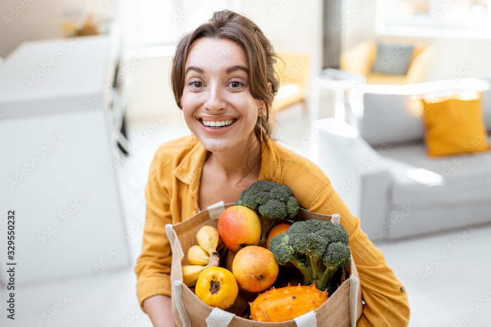 一位年轻开朗的女士拿着装满新鲜水果和蔬菜的购物袋站着的肖像