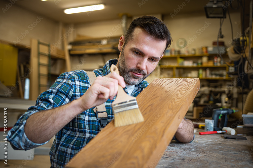 工匠在木工车间用画笔在木板上涂清漆