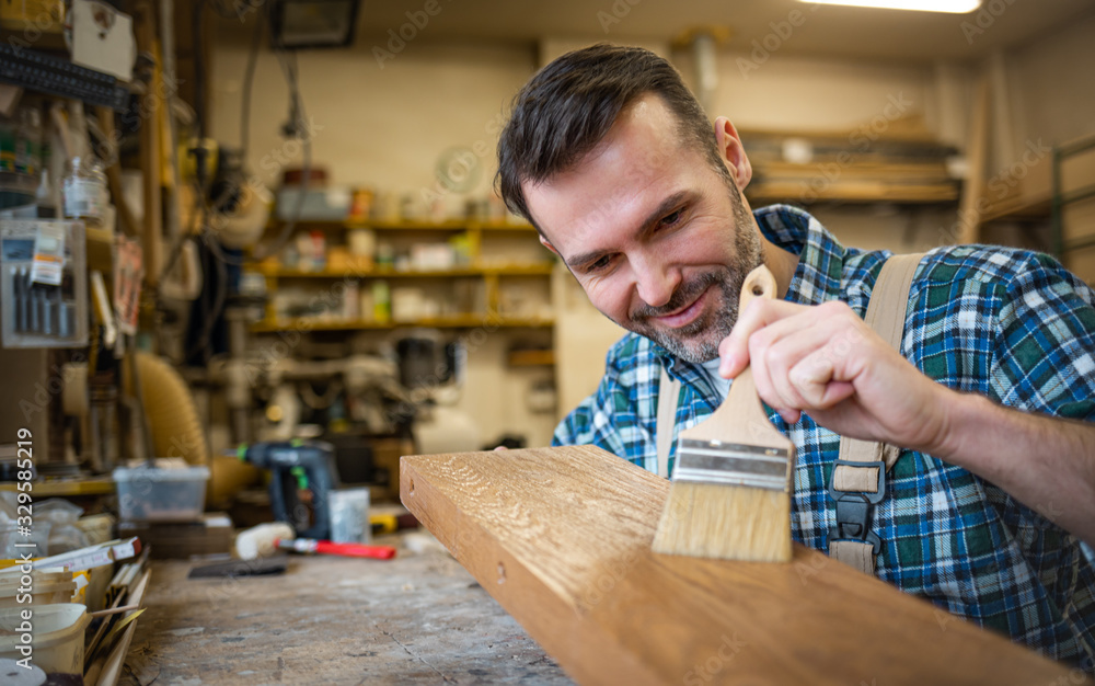 Craftsman applies varnish on wooden board by paintbrush in his carpentry workshop