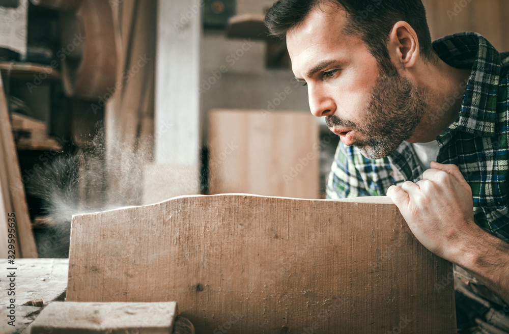 Carpenter blowing sawdust off wooden board in craft workshop